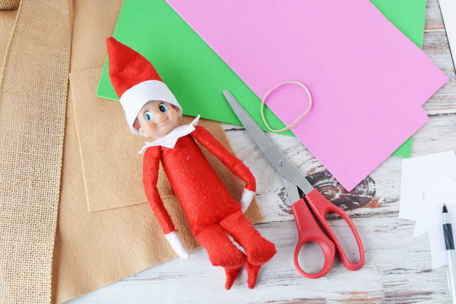 elf on the shelf doll laying on top of felt and foam sheets with scissors