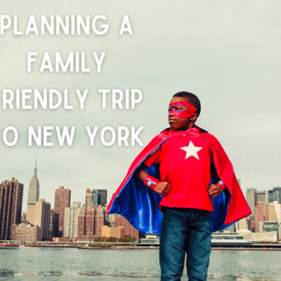 boy in superhero cape and mask standing across river from new york city