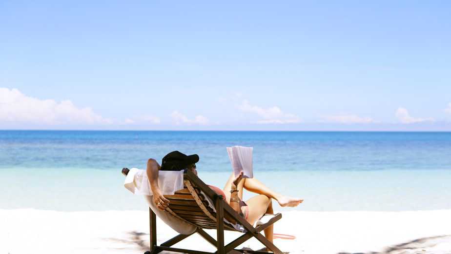 woman with beach hat sitting in chair reading on beach
