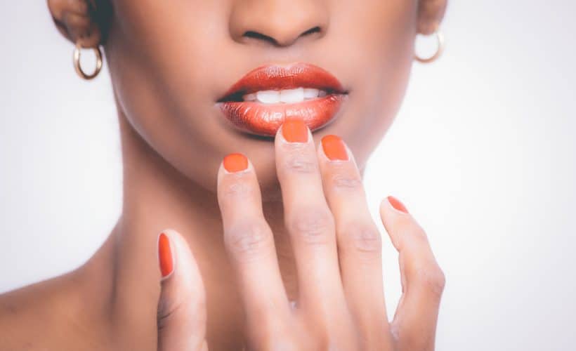 woman with orange manicure touches lips