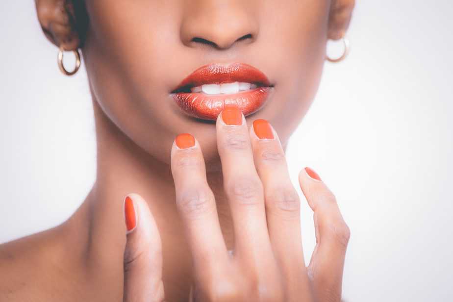 woman with orange manicure touches lips 