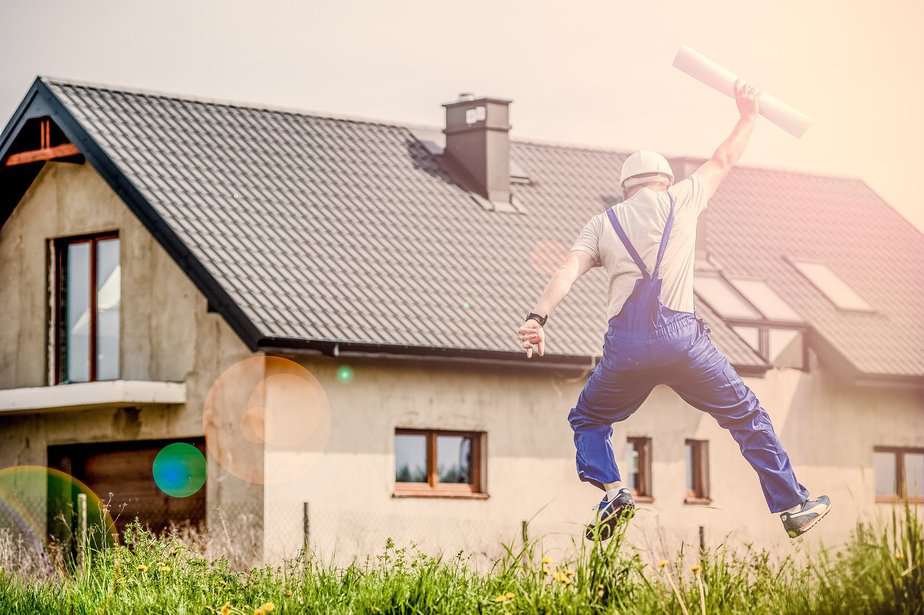 man in overalls jumping in the air near house