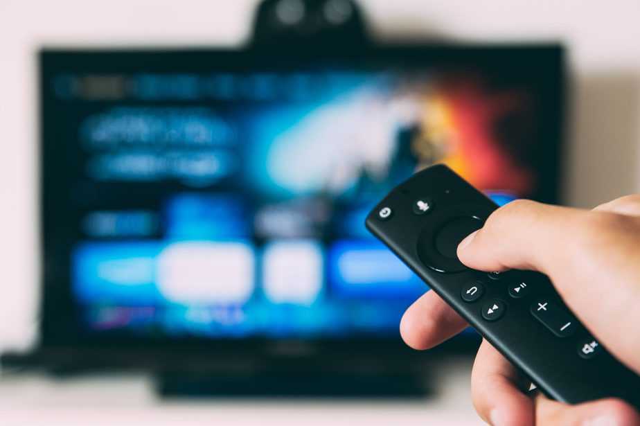 close up of finger pressing remote control button for tv which is in background