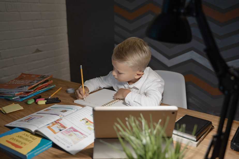 boy in white shirt doing schoolwork at table