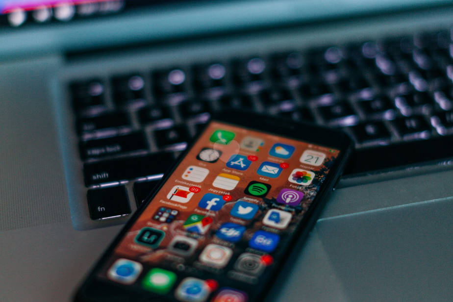 smart phone with several social media apps on screen sitting on top of an open laptop