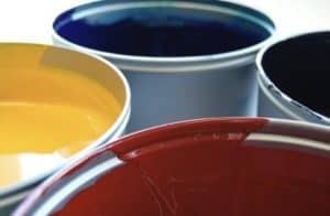 Close up of the top of four open paint cans filled with red yellow blue green paint