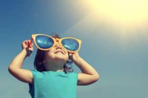 Young toddler wearing sleeveless shirt and enormous silly plastic sunglasses looking up at the sky 