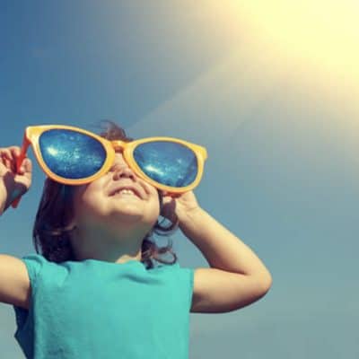 Young toddler wearing sleeveless shirt and enormous silly plastic sunglasses looking up at the sky