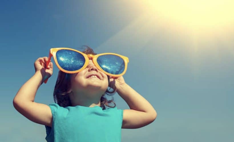 Young toddler wearing sleeveless shirt and enormous silly plastic sunglasses looking up at the sky